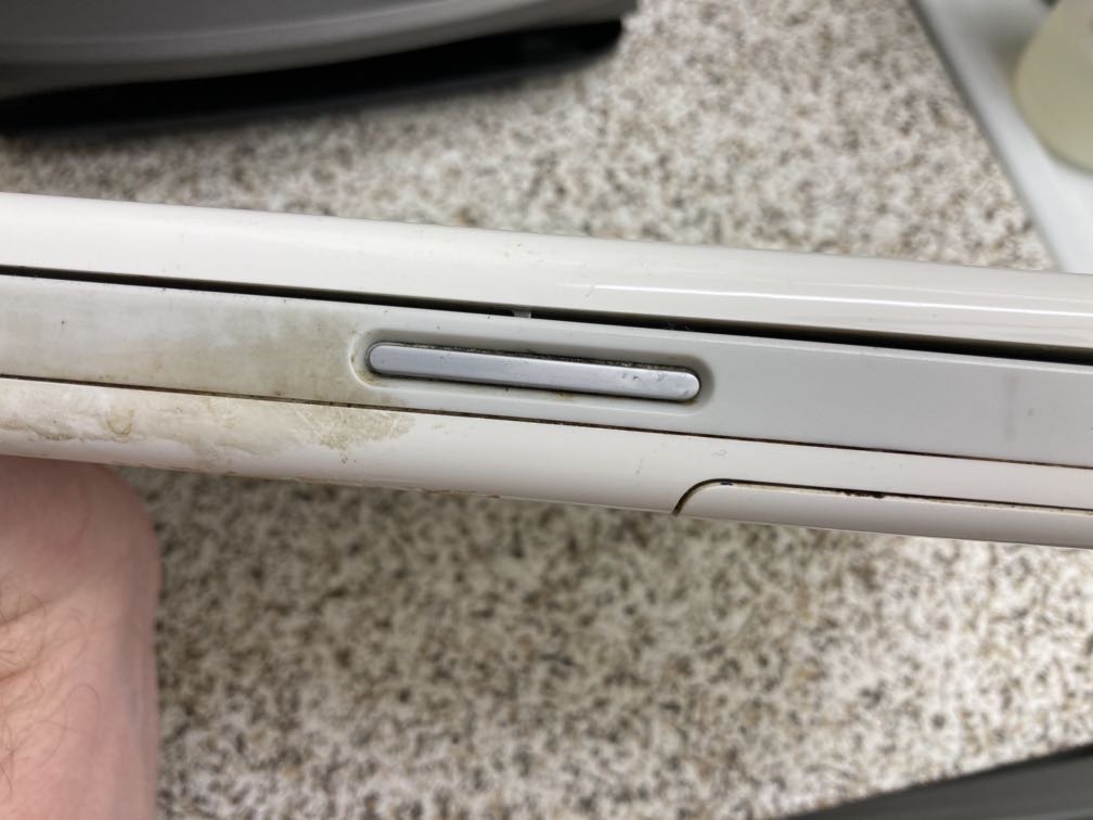 Photo of the front edge of the machine. To the left of the latch release button, I haven't cleaned yet, and there's a visible beige patina. To the right of the button, my cleaning has revealed mostly-pristine-looking gray and white plastic.