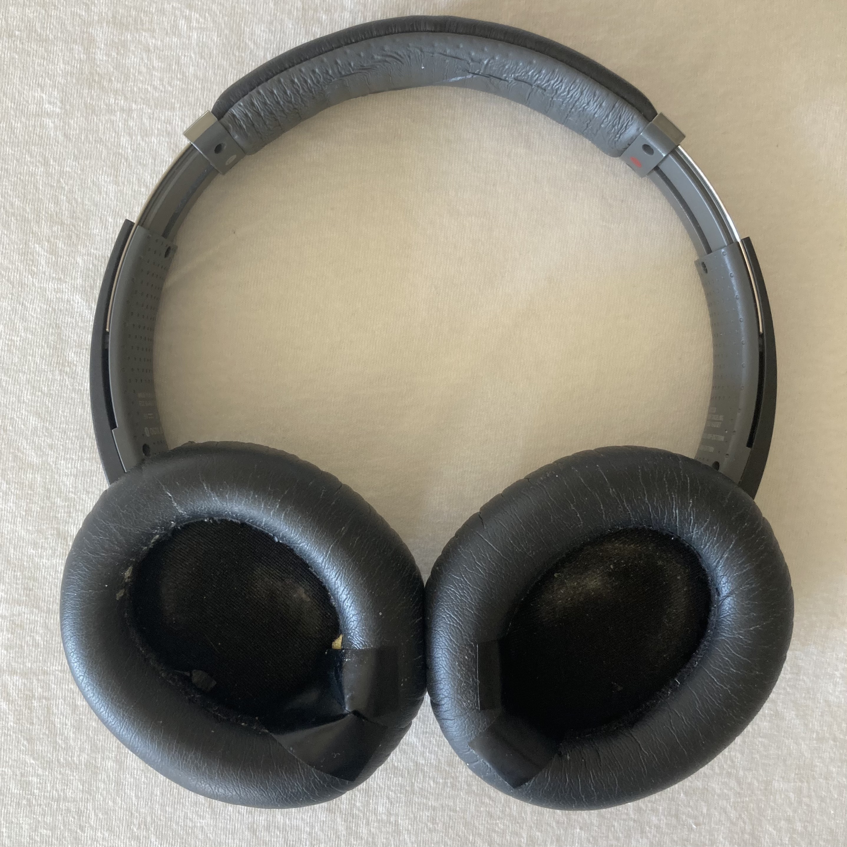 The stock earpads have each developed a hole along the bottom curve, exposing the foam inside. Each hole is vainly patched over with poorly-sticking electrical tape.