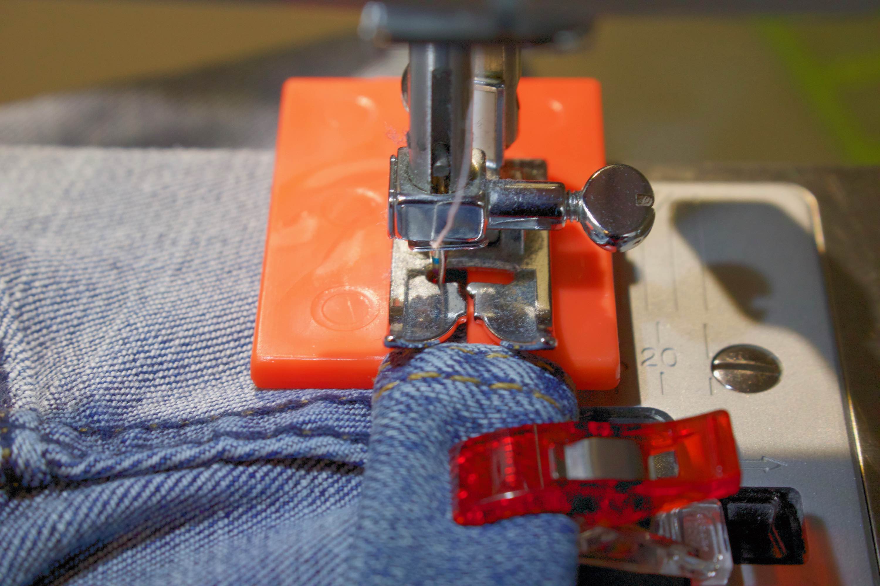 Close-up photo of a sewing machine foot on a Jean-a-ma-jig on the far side of an inseam on the way onto it…